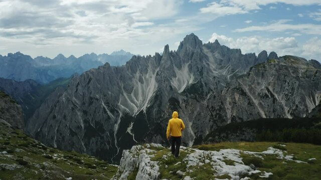 Aerial view of man in yellow coat in front of Auronzo di Cadore of Cadini di Misurina mountains group in Dolomites, Italy, part of Tre Cime di Levaredo national park and UNESCO world heritage site.