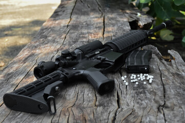 Obraz premium Close up view of black long barreled automatic rifle or bb gun on wooden floors with white plastic bullets. Soft and selective focus.