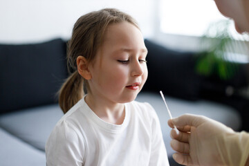 Using cotton swab while testing little girl at rapid COVID-19 test at home
