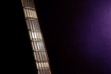 The neck of an acoustic guitar on a blurred, dark, purple background, fragment.