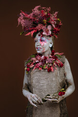 A girl smeared with clay in a cemented dress. The model has a headdress made of flowers.