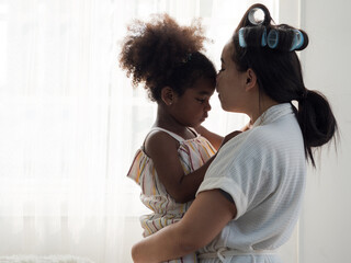 Asian mother holding cute mixed race African daughter and kissing on the forehead on white background.