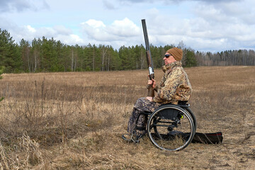 hunter in a wheelchair and camouflage with gun in his hands against the background of the forest...