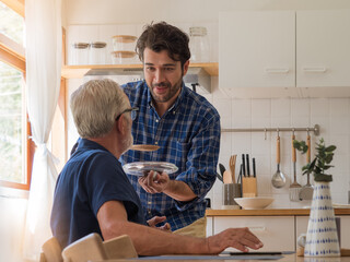 Father and son spend quality time together. Son cooks food for senior father to taste in the kitchen at home.
