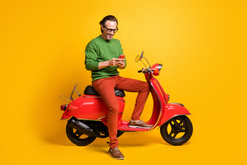 Fototapeta na wymiar Photo of man hold phone ride scooter wear spectacles green sweater trousers shoes isolated yellow color background