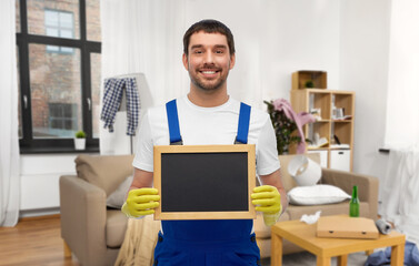 profession, cleaning service and people concept - happy smiling male worker or cleaner showing chalkboard over home room background