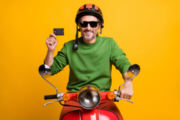 Photo of man drive cycle demonstrate debit card wear helmet eyewear green pullover isolated yellow color background