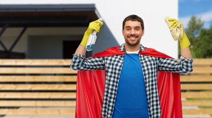 cleaning and people concept - happy smiling man in superhero cape and rubber gloves with rag and detergent over living house background © Syda Productions