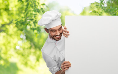 cooking, culinary and people concept - happy smiling male chef in toque with big white board over green natural background