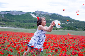 The kid is happy in the nature have fun in the field with poppy red flowers. Girl collect flowers in summer vacation