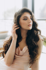 Beautiful, stylish, and elegant girl brunette, model, with makeup and curly hair in a peach-colored silk dress for a magazine photoshoot in fashion style.