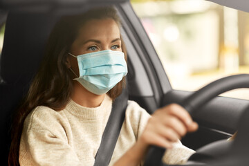 Fototapeta na wymiar safety and people concept - young woman or female driver in medical mask driving car in city