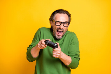 Photo of crazy excited man hold controller play game open mouth wear specs green sweater isolated yellow color background