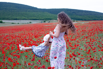 Mother and daughter resting in the field with poppy flowers and collect them. The woman and girl...