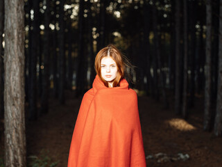 A woman with a red plaid on her shoulders among the trees in the forest