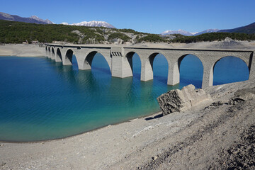 old stone bridge and snow covered mountains  on Serre Ponçon lake, France