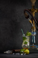 Hookah (shisha) and glass of Mojito cocktail with lime and ice on dark grey background. Weekend or...