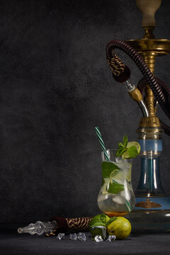 Hookah (shisha) and glass of Mojito cocktail with lime and ice on dark grey background. Weekend or holiday party. Hookah bar