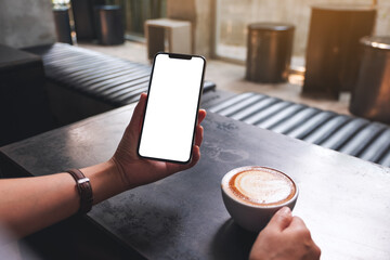 Mockup image of a woman holding mobile phone with blank white desktop screen while drinking coffee