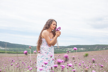 Happy woman in sundress walking in the field with wild flowers and make the bouquet