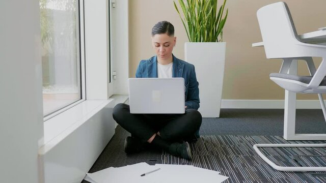 Businesswoman sitting cross-legged in ofice, using laptop