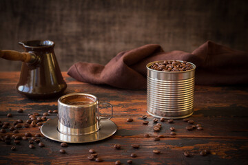 Steel cup of coffee, blended coffee beans in a tin can and ceramic turka, brown napkin on a dark...