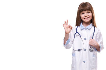 Cute little girl doctor wearing white coat holds stethoscope and shows OK gesture on white isolated background