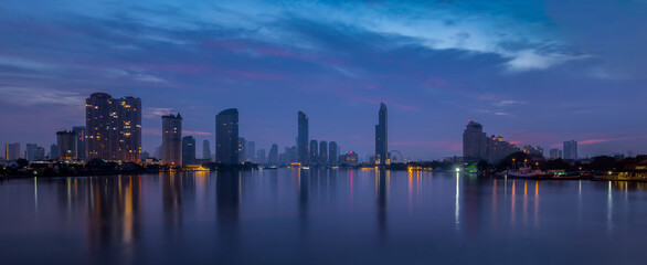 Panorama view of Ferris Wheel and business district in Bangkok city with water reflection at twilight time.