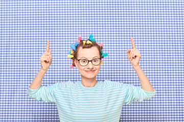 Happy girl with hair curlers on head is pointing at copy space
