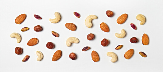 Different types of nuts scattered on isolated white background. Nutrient dense vegan snacks. Clean eating concept. Close up, copy space for text, top view, flat lay.