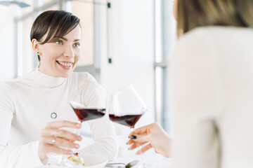 Happy girlfriends toasting in restaurant. Woman drinking red wine, saying cheers in a bar or restaurant