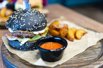 Burger with black bun. Beautiful serving of a burger with potatoes. A real non-photoshopped burger.