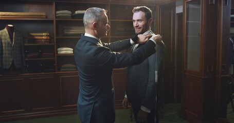 Cinematic shot of professional tailor taking measurements of client for creation custom tailored suit in a luxury tailoring atelier. Concept of fashion, handmade, hand craft, couturier and business.	 - obrazy, fototapety, plakaty