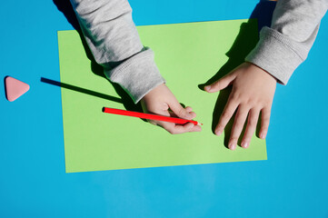 children's hands with a pencil top view. child draws a table top view. space for text.