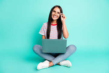 Full size photo of nice optimistic lady work laptop sit wear spectacles t-shirt jeans sneakers isolated on teal color background