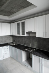 Modern minimalism style kitchen interior in monochrome tones. Custom kitchen with grey white facadesmdf and dark grey countertop with installed kitchen hood and sink. Modular kitchen from chipboard.