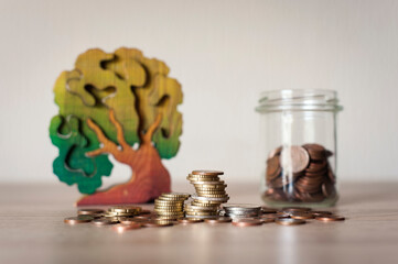 Unas pilas de monedas, un bote de cristal lleno de monedas y un árbol de madera
