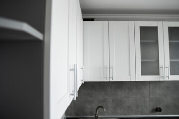 Modern minimalism style kitchen interior in monochrome tones. Custom kitchen with grey white facadesmdf and dark grey countertop with installed kitchen hood and sink. Modular kitchen from chipboard.