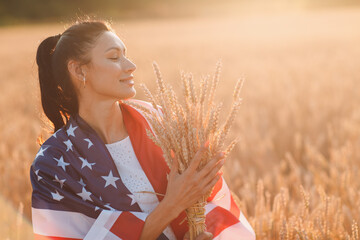 Woman with American flag and with a sheaf of ears in wheat field at sunset. 4th of July....