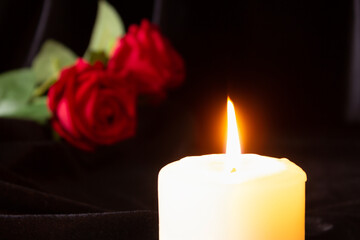 A burning candle and a red rose on a black background. The concept of condolences, mourning, and funerals.