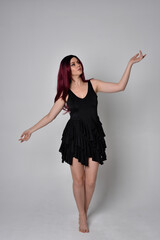 
Full length portrait of a red haired  girl wearing black dress and feather angel wings.  Standing...