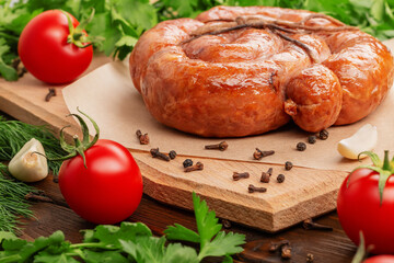 Side view of smoked homemade sausage tied with a whip spiral on a wooden cutting board. Tomatoes,...