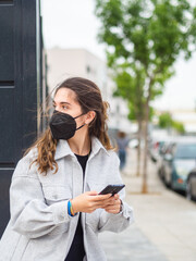 Mujer joven con mascarilla usando y hablando por su teléfono móvil cumpliendo las medidas de...