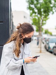Mujer joven con mascarilla usando y hablando por su teléfono móvil cumpliendo las medidas de seguridad y distanciamiento social de la pandemia del coronavirus