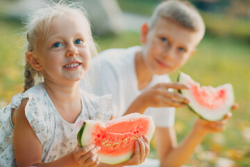 Funny little toddler kids brother and sister eating watermelon on the park. Happy boy and girl together. Childhood, Family, Healthy Diet Concept.