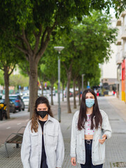 Mujeres jóvenes amigas paseando por la calle con mascarilla para protegerse del coronavirus 