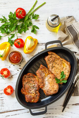Barbecues parties menu. Baked meat pork loin on the bone with spices in a cast iron pan on rustic wooden table. Top view flat lay.