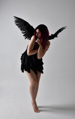 
Full length portrait of a red haired  girl wearing black dress and feather angel wings.  Standing...