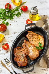 Barbecues parties menu. Baked meat pork loin on the bone with spices in a cast iron pan on rustic wooden table. Copy space.