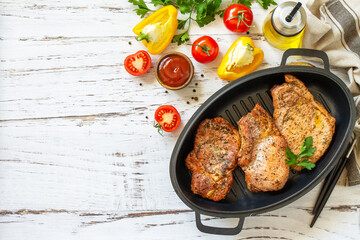 Barbecues parties menu. Baked meat pork loin on the bone with spices in a cast iron pan on rustic wooden table. Top view flat lay. Copy space.